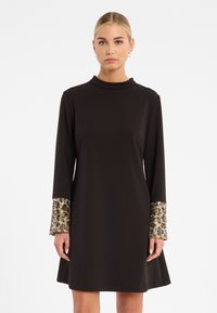 Schwarz langärmliges Kleid mit hohem Kragen, ausgestattet mit strukturierten goldenen und blauen gemusterten Manschetten und einem ausladenden Rock. Glattes Material.