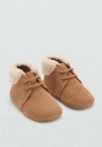 Bruna mockaskor med en mjuk krämfärgad fleecefoder, kort skaft och korsade snören, vilket ger en mysig design och en bekväm passform.