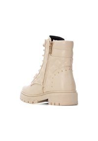 Botas de tobillo de cuero beige con un diseño texturizado, cremallera lateral y tachuelas doradas. Suela robusta y cuello acolchado para mayor comodidad y soporte.
