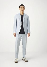 Hele hall sinine lina ülikond, millel on klappidega krae, ühe nupuga kinnitamine ja kaks taskut; kombineeritud musta särgi ja mugavate spordijalanõudega.