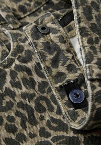 Leopardskinnsmönstrad tyg med nyanser av brunt och svart, med en knappdetalj och synlig söm på en texturerad yta.
