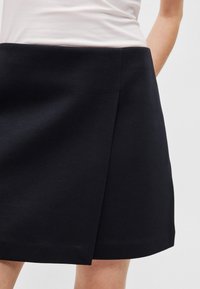 Zwarte A-lijn rok met een gladde textuur, voorzien van een zijsplitdetail en een platte tailleband. Gemaakt van een mix van katoen en polyester.