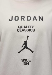 White cotton t-shirt featuring black text: "JORDAN QUALITY CLASSICS SINCE 1984" and a silhouette of a jumping figure.