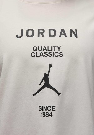 T-shirt en coton blanc avec un texte noir : "JORDAN QUALITY CLASSICS SINCE 1984" et une silhouette d'une figure en train de sauter.