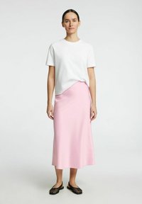 T-shirt en coton blanc associé à une jupe midi en satin rose pâle. Des chaussures tissées noires complètent la tenue. Design simple et épuré.