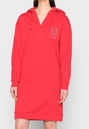 Nainen, jolla on päällään punainen hupullinen mekko, jossa on pitkät hihat ja vasemmassa rinnassa "AX Armani Exchange" -logo.