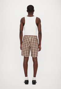 Brown and cream plaid shorts with an elastic waistband, back pockets, and a relaxed fit, paired with a white sleeveless shirt.