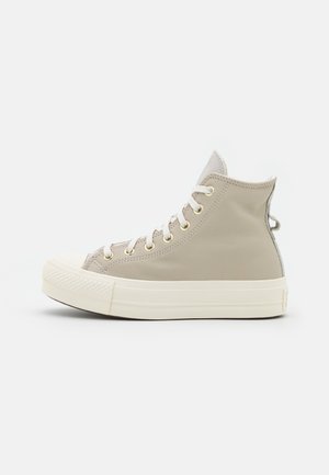 Beige hoge sneakers met witte veters, een ronde rubberen neus en een dikke off-white zool, zijaanzicht.