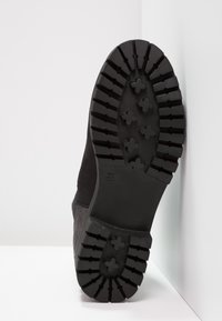 Suela de bota negra con profundas estrías y un diseño robusto, hecha de goma con una superficie texturizada para un mejor agarre. Talla 37 indicada.
