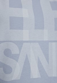 Šviesiai mėlyna medžiaga su didelėmis, nereguliariomis baltomis raidėmis. Tekstūra atrodo minkšta ir lygi, su subtiliu blizgesiu.