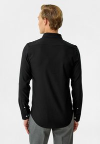 Zwarte langwerpige shirt met lange mouwen, gemaakt van een gladde stof, met een klassieke kraag, knoopmanchetten en een gebogen zoom aan de achterkant.