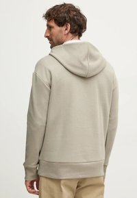 Felpa leggera beige chiaro con cappuccio, caratterizzata da un tessuto testurizzato, vestibilità rilassata e polsini e orlo a coste. Design semplice senza motivi.