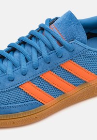 Blå semsket sneakers med oransje striper, mesh-paneler og en gummiruggsåle. Har runde lisser og en polstret tunge.