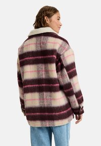 Rutet jakke i creme, burgunder og lyserøde nuancer. Blødt stof med sherpa-krave, oversized pasform og sænkede skuldre seams.