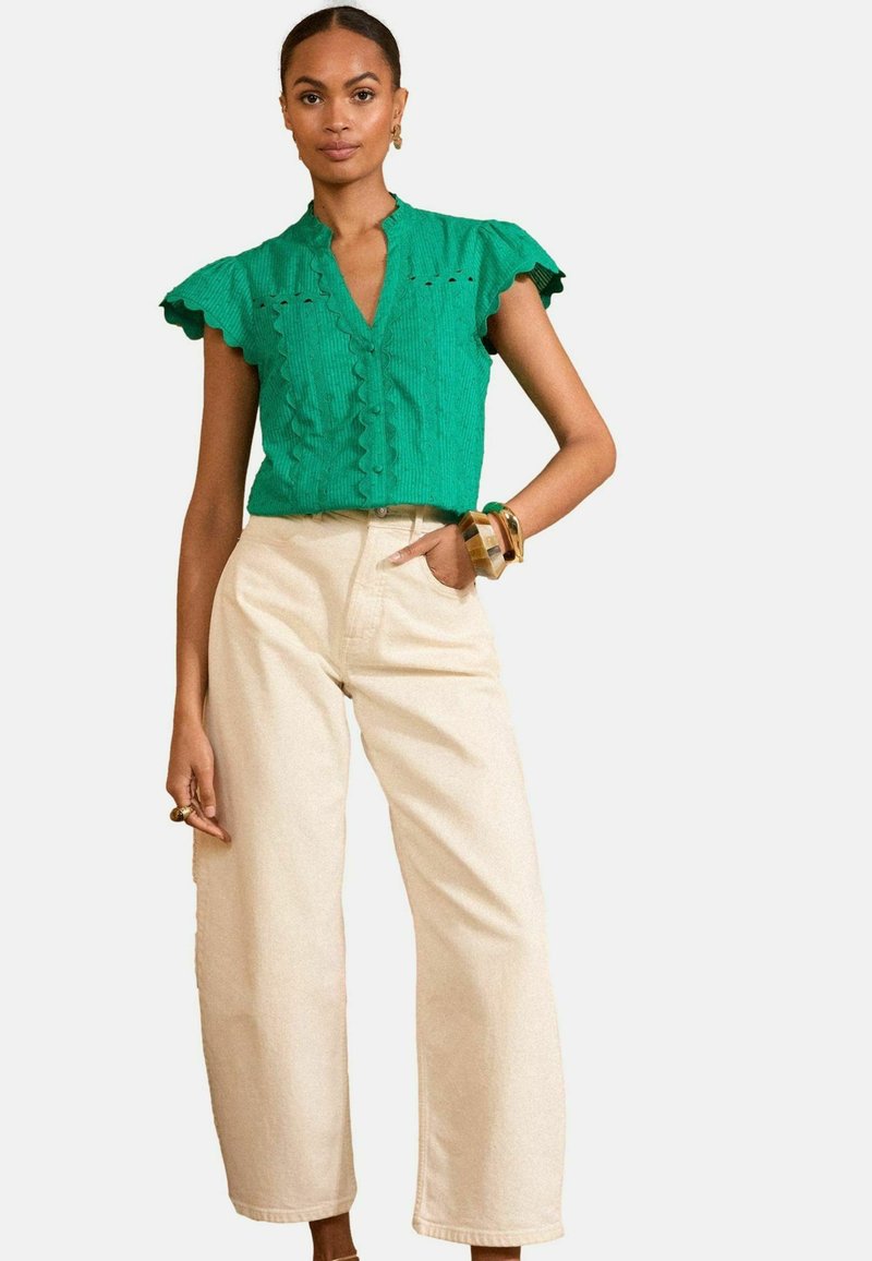 Green textured top with ruffle sleeves and a v-neckline, paired with cream-colored wide-leg pants. Notable button detail on the top.