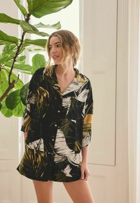 Conjunto de camisa de manga corta y pantalones cortos con base negra y estampados de hojas tropicales en verde y dorado; tela suave con un corte holgado.