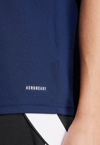 Dunkelblaues AEROREADY Sportshirt mit glatter Textur, versehen mit einem weißen Logo in der Nähe des Saums, kombiniert mit schwarzen Shorts und weißen Akzenten.