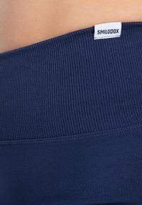 Marineblauwe ribgebreide tailleband met een gladde textuur, voorzien van een klein wit label met "SMILODOX" in zwarte tekst.