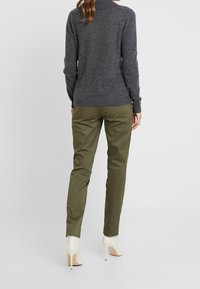 Un pull gris en tricot avec un col montant, associé à un pantalon slim olive vert et des chaussures à talons blancs, vu de dos.