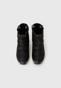 Par de sapatos pretos isolados, tipo slip-on, com cordões elásticos e solas brancas, vistos de cima sobre um fundo branco.