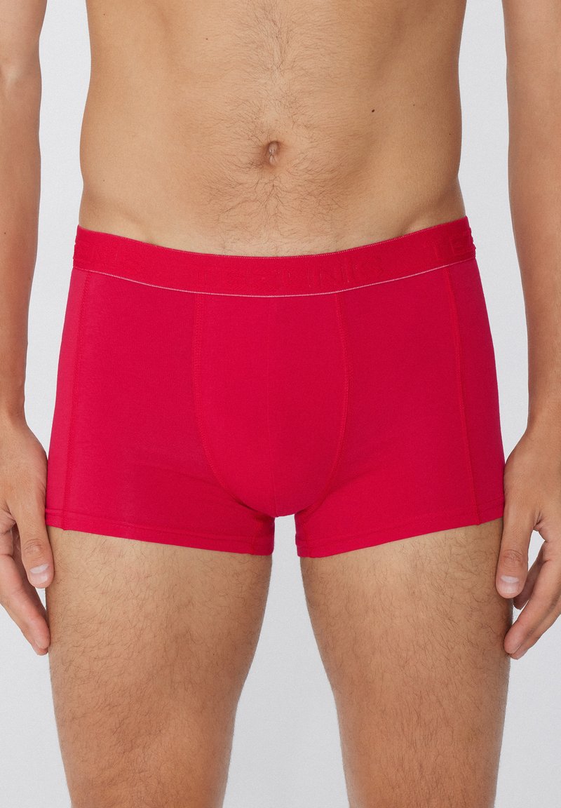 Červené boxerky vyrobené z elastického materiálu s elastickým pasem, s hladkou texturou a prošíváním na přední straně a po stranách.