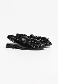 Schwarze Lacklederschuhe mit Slingback und flacher Sohle, mit fransigen Kanten und einem dekorativen Quastenakzent an der Vorderseite.