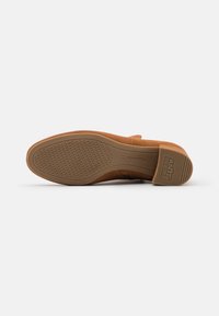 Zapato de ante marrón tumbado de lado, mostrando una suela de goma con textura antideslizante y una etiqueta "ANTI SLIDE" en el talón.