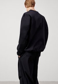 Felpa nera a maniche lunghe con scollo a girocollo e vestibilità comoda, dotata di polsini a coste e texture liscia. Design minimalista, senza logo visibile.