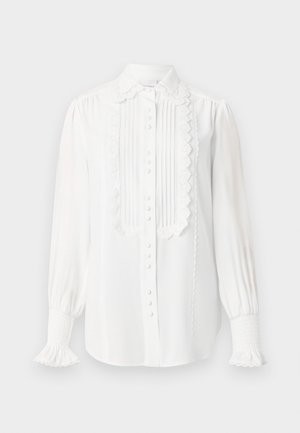 Valkoinen pitkähiha blouse pitsireunalla, pleatattu etupaneeli, kankaasta päällystetyt napit ja rypytetyt hihansuut röyhelöillä.