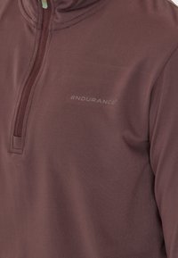 Mørkerød zip-neck pullover lavet af glat stof, med et subtilt logo og et halv-zip design for ventilation. Blød tekstur og tætsiddende form.