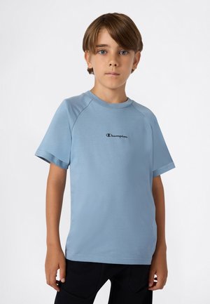 Camiseta de manga corta azul claro hecha de tejido suave, con cuello redondo y un pequeño logo negro de "Champion" en el pecho.