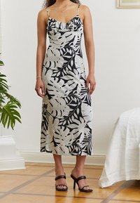 Robe florale noire et blanche avec bretelles spaghetti, encolure à volants et silhouette ajustée ; associée à des sandales à talons hauts noires.
