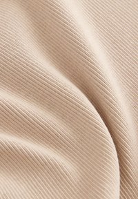 Beige ribbelstof met een zachte textuur, met verticale lijnen en zachte plooien, wat wijst op een lichtgewicht materiaal dat geschikt is voor kleding.
