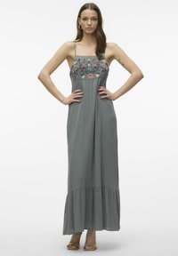 Maxiklänning i mjukt grått tyg med blommönster på bodice, spaghettiremmar och ett utsvängd slut. Slät textur och flödande design.