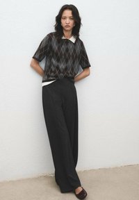 Pulover scurt cu mânecă, cu un model argyle negru și gri, cu guler alb, asociat cu pantaloni largi negri cu talie înaltă și pantofi dark.