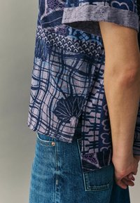 Lühikeste varrukatega, mustriga shirt sinise ja lillaka tooni variatsioonides, millel on geomeetrilised kujundid ja mugav lõige, koos teksapükstega.