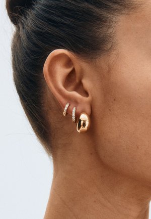 Zelta metāla auskari ar gludu, noapaļotu dizainu un diviem mazajiem spīdīgiem stīpas akcentiem ar caurspīdīgiem akmentiņiem.