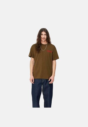 Camiseta de algodón marrón de manga corta y cuello redondo, con un pequeño gráfico rojo en el pecho. Combinada con unos vaqueros azules holgados.