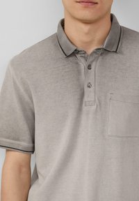 Grijze polo shirt met een gestructureerde afwerking, twee knopen bij de hals, korte mouwen en een borstzak. Kenmerkt zich door een contrasterende donkere afwerking op de kraag.