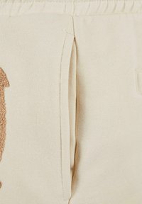 Beige sweatshirt material with a side pocket, featuring a textured brown graphic design. The fabric has a soft, brushed finish.