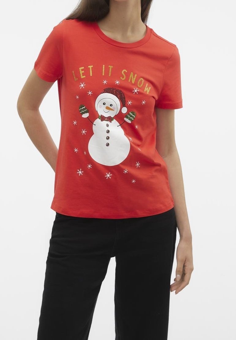 Femme portant un t-shirt rouge à manches courtes avec un bonhomme de neige, des moufles, des flocons de neige et le texte "LET IT SNOW" en lettres dorées.