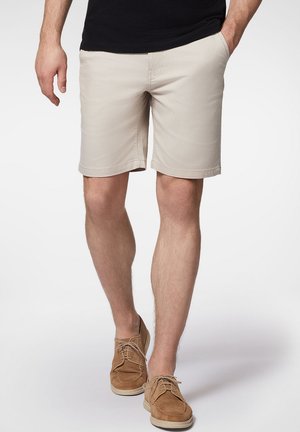 Beżowe szorty z bawełny z bocznymi kieszeniami, prostym krojem i podwiniętymi brzegami. Połączone z jasnobrązowymi zamszowymi butami i czarnym t-shirtem.