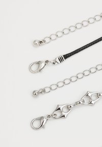 Tre catene d'argento di diversi design: una con un anello rotondo, una con una treccia nera texture e una con un anello unico come accentuazione. Ognuna ha un gancio.