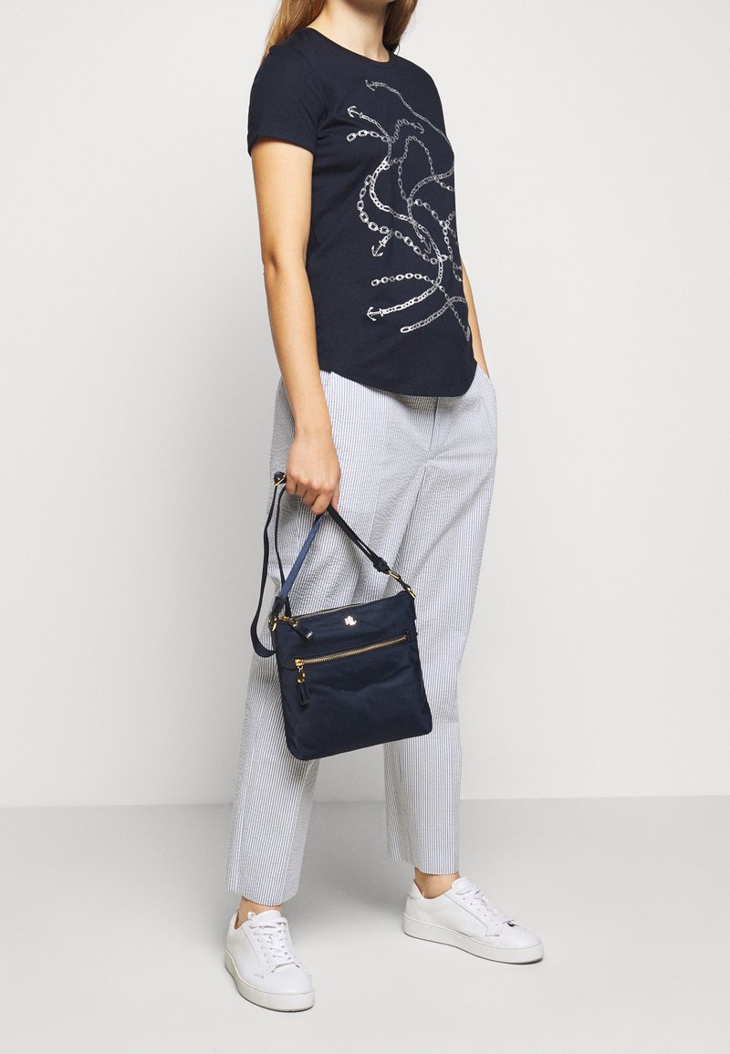T-paita tummansinisellä värillä ja hopealla graafisella suunnitelmalla, yhdistettynä vaale-striped-housuihin, valkoisiin lenkkareihin ja pieneen tummansinsiseen käsilaukkuun.