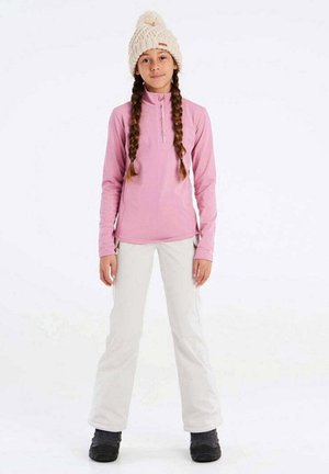 Rosa Langarmshirt mit Reißverschluss am Hals, kombiniert mit weißen Hosen. Beiger Strickbeanie mit einem Pompon, schwarze Schneestiefel. Glatte Textur, lässige Passform.
