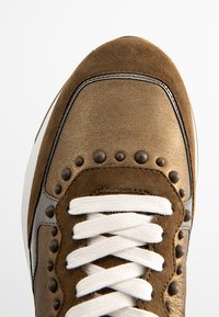 Braune Sneaker mit einem Obermaterial aus Leder und Wildleder, weißen Schnürsenkeln, metallischen Akzenten und Nietenverzierungen an den Seiten.