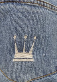Denim fabric featuring a light blue background with a white embroidered crown design. The crown includes three peaks and a horizontal base.