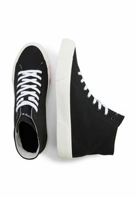 Zapatillas altas negras de lona con cordones blancos, suelas de goma y detalles de costura mínimos, que presentan una etiqueta de logo en la lengüeta.