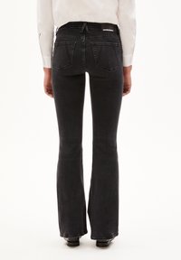 Black flared jeans with a high waist, featuring two back pockets and a stamped logo on the waistband. Smooth denim texture.