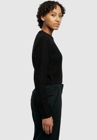 Maglione nero corto con un design a maglia testurizzata, maniche lunghe e polsini a coste, abbinato a pantaloni neri a vita alta.